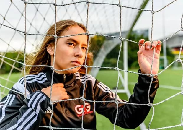 A Goals 4 Girls player in a tracksuit leaning against a goal net
